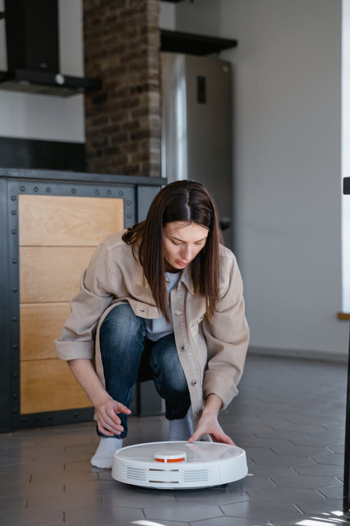 Woman adjusting a robotic vacuum cleaner on a tiled floor indoors.